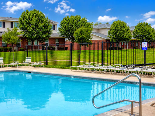A swimming pool surrounded by a black fence and lawn chairs.