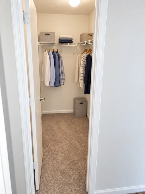 A white closet with clothes hanging up and a trash can.