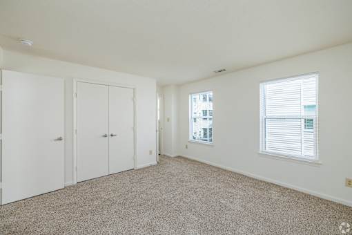 A room with white walls and carpeted floor with three white doors.