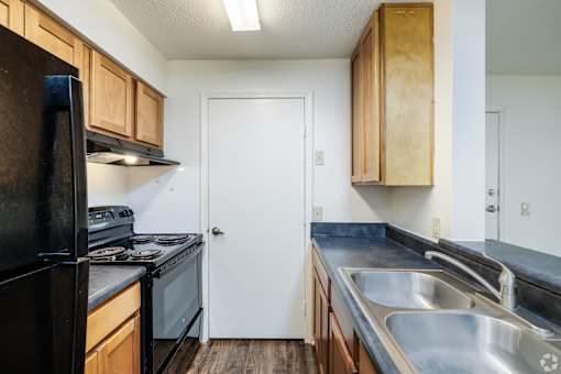 A kitchen with a black refrigerator, wooden cabinets, and a white door.