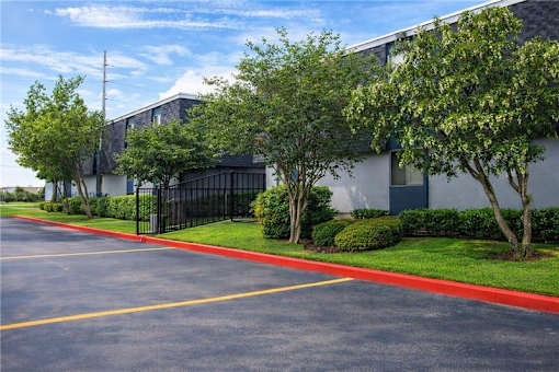 A parking lot in front of a building with a black fence and green trees.