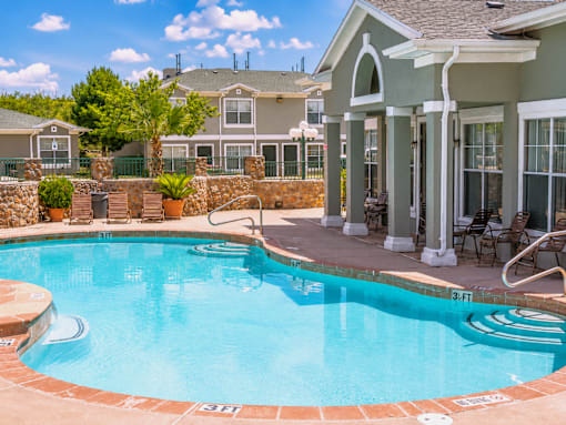 A pool with a stone border and a house in the background.