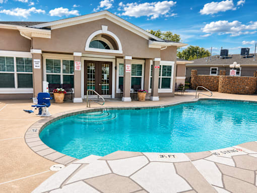 A swimming pool in front of a house with a blue sky in the background.