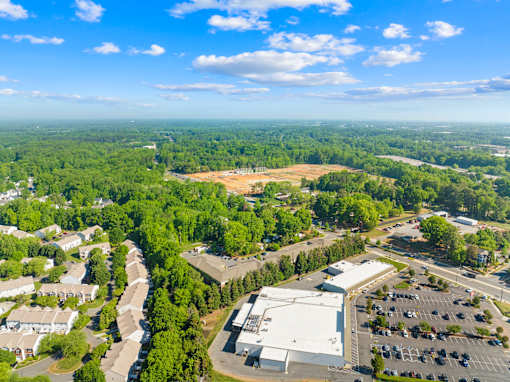 A large white building is surrounded by a parking lot and trees.