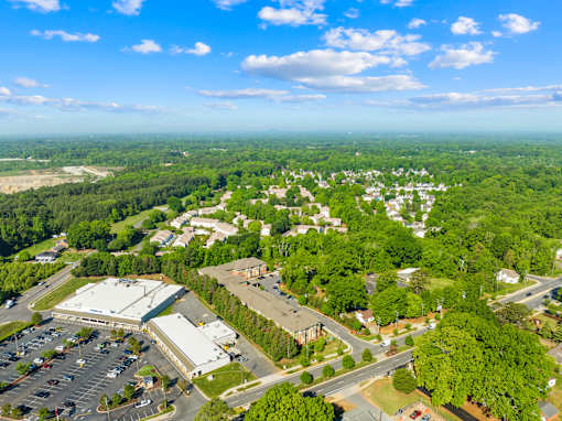 A large white building is surrounded by a parking lot and trees.
