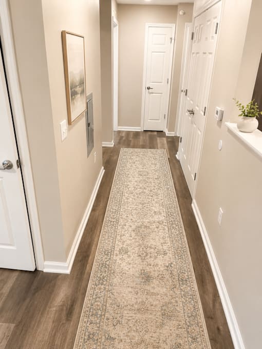 A hallway with a rug on the floor and a painting on the wall.