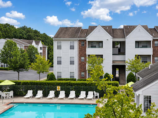 A pool in front of a white and brick building with a yellow umbrella.