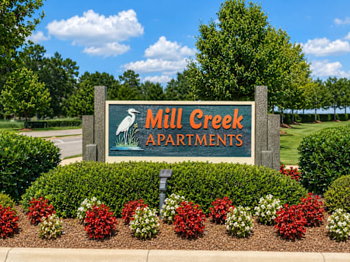 A sign for Mill Creek Apartments is surrounded by flowers and greenery.