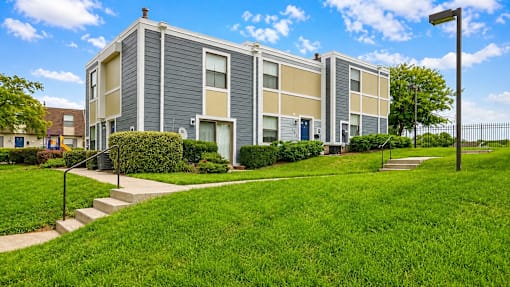 A modern building with a grey and beige facade is surrounded by a well-kept lawn and a clear blue sky.