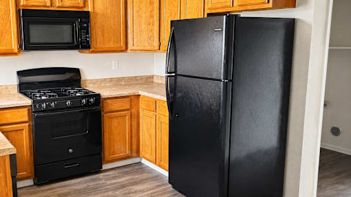 A black refrigerator stands in a kitchen with wooden cabinets and a black stove.