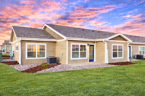 A house with a brown roof and tan siding is shown with a blue sky in the background.