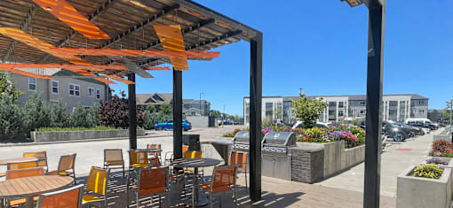 A patio with orange chairs and tables under a striped awning.