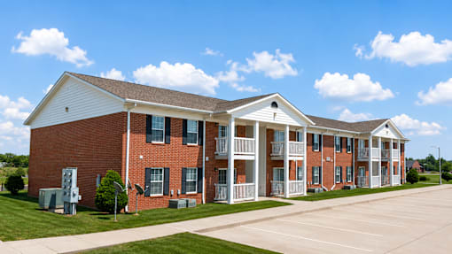 A red brick building with white trim and a parking lot in front.