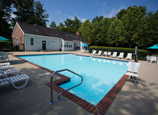 A pool with a red brick border and white chairs around it.