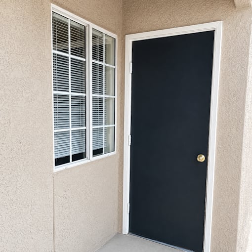 A black door with a gold knob is on the right and a window with white blinds is on the left.