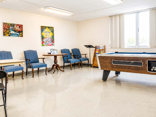 A room with a pool table and chairs.