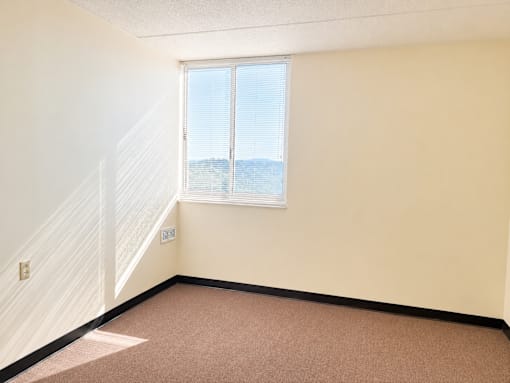 A room with a carpeted floor, a window with blinds, and a staircase with a white railing.
