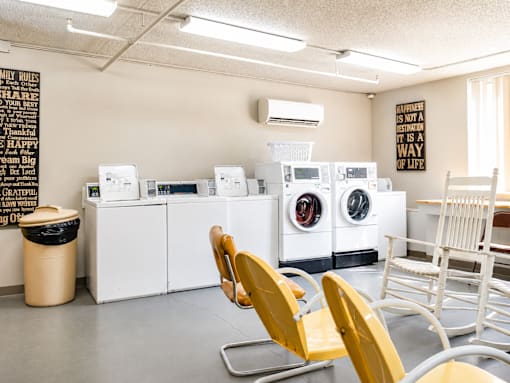 A laundromat with washers and dryers and chairs.