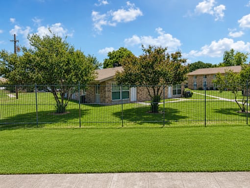 A grassy area with a building in the background and a fence in the foreground.