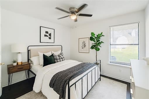A bedroom with a bed, a ceiling fan, and a window with blinds.