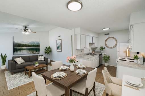 A well-lit, modern kitchen and dining area with a grey sofa and a painting of a lake on the wall.