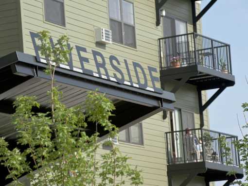 A balcony with a metal railing and a tree in front of a building with the word "Everside" on it.