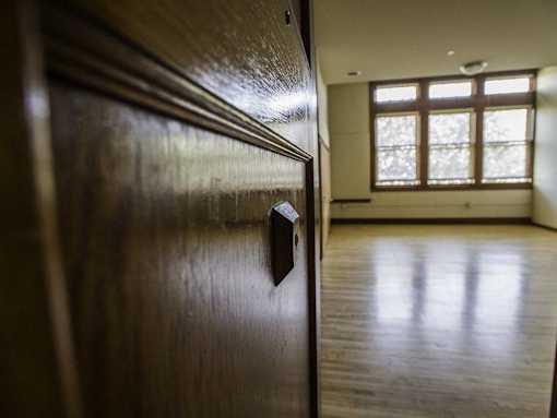 A dark wooden door with a handle in the foreground and a brightly lit room in the background.
