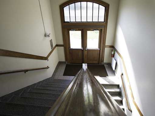 A wooden staircase with a carpeted runner leads to a door with a window above it.