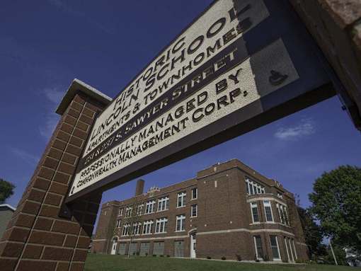 A sign for the historic school is displayed in front of a brick building.