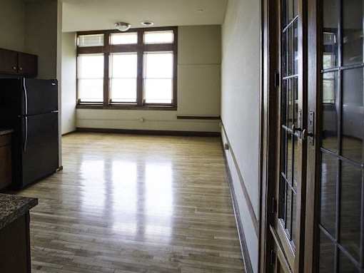 A room with a black fridge and wooden flooring.
