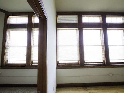 Two windows with blinds in a room with wooden beams.