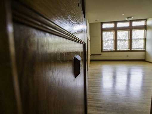 A dark wooden door with a handle in the foreground and a brightly lit room in the background.