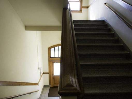A staircase with a wooden handrail and a door at the bottom.