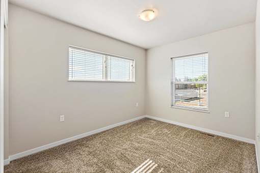 A room with beige carpet and two windows with blinds.