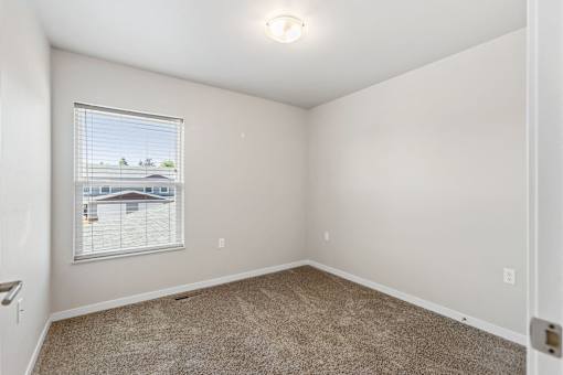 A room with a carpeted floor and a window showing a view of a house.
