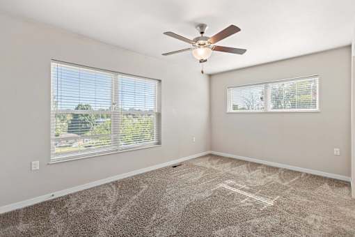 A room with a ceiling fan and two windows.