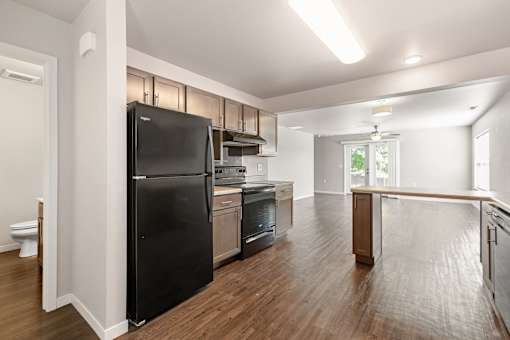 A black refrigerator in a kitchen with wooden floors and white walls.