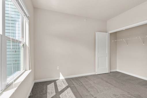 A room with a carpeted floor, a white door, and a window with blinds.