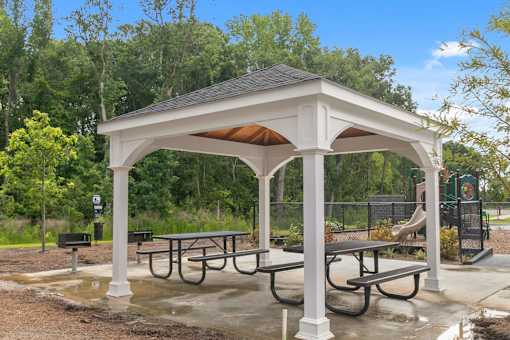 A white gazebo with a brown roof is surrounded by picnic tables.