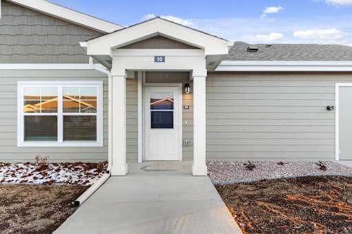 A house with a grey siding and a white door is numbered 10.