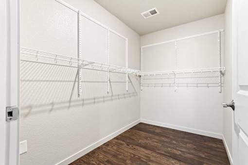 A walk-in closet with white shelving and a wooden floor.