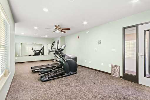 A room with a row of treadmills and a fan on the ceiling.