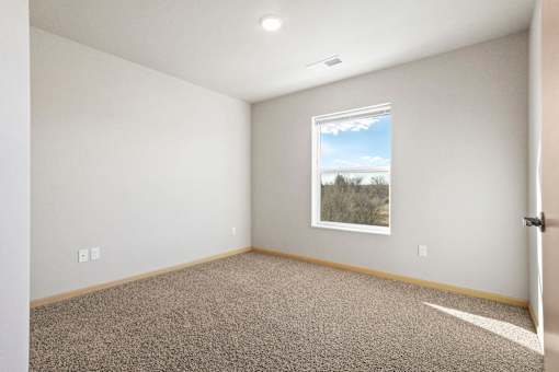 A room with a carpeted floor and a window showing a view of trees and sky.