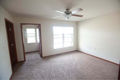 A room with a ceiling fan and two windows.