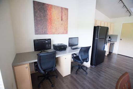 A room with a desk, chairs, and a fridge.