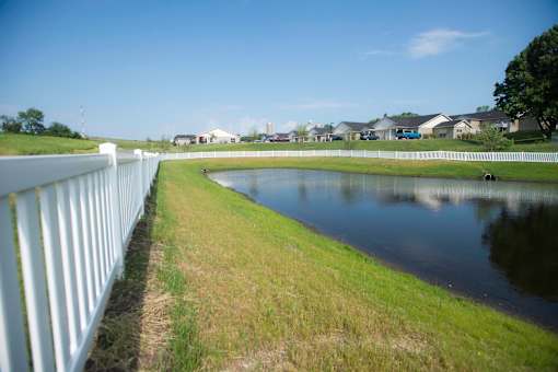 A white fence runs along the edge of a grassy field with a pond in the middle.
