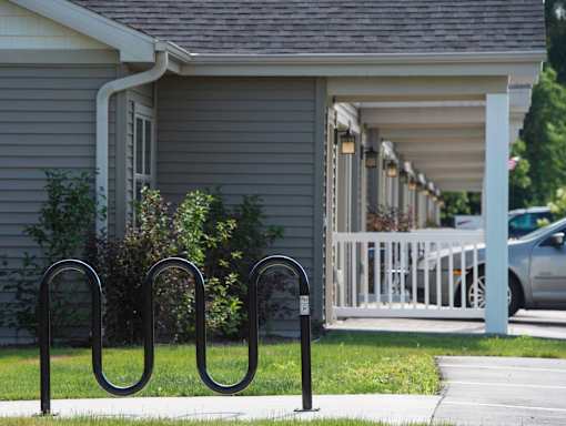 A black metal bike rack sits in front of a grey house.