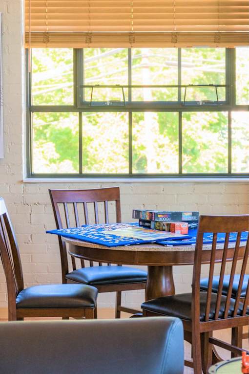 A table with chairs and a book is in front of a window.