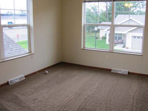 A room with a carpeted floor and two windows.