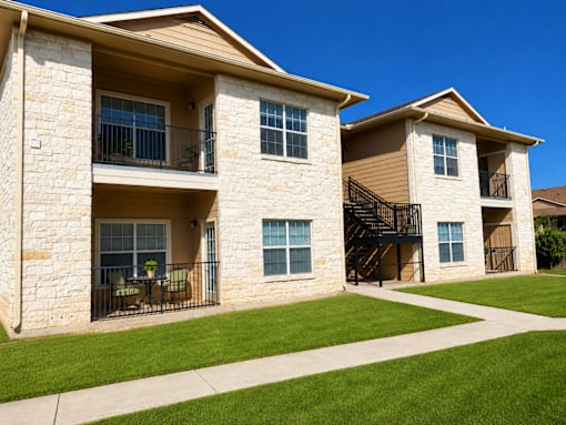 Two tan stone houses with black railings and green lawns.